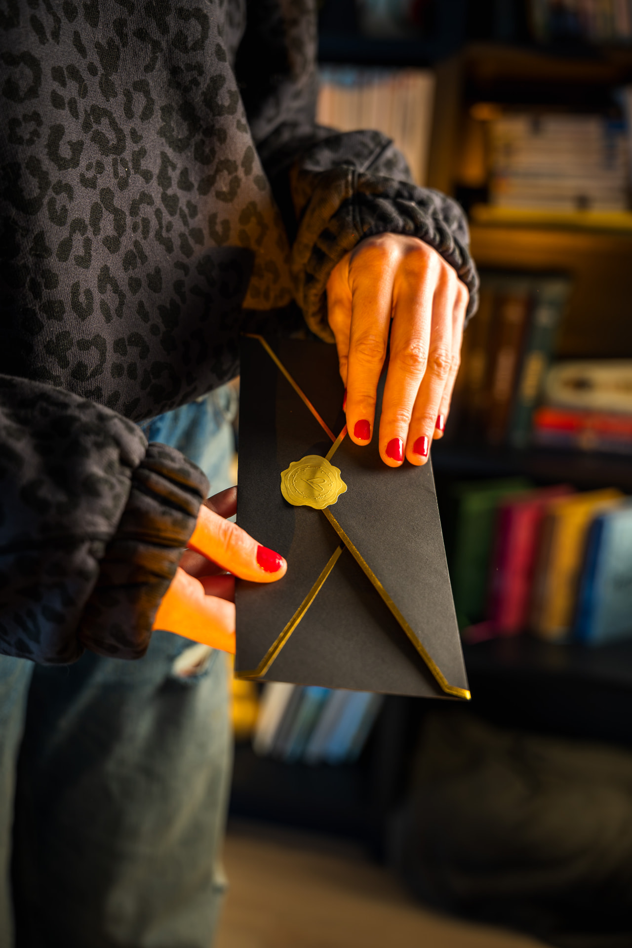 Enveloppe cadeau noire scellée d'un cachet doré, tenue entre les mains