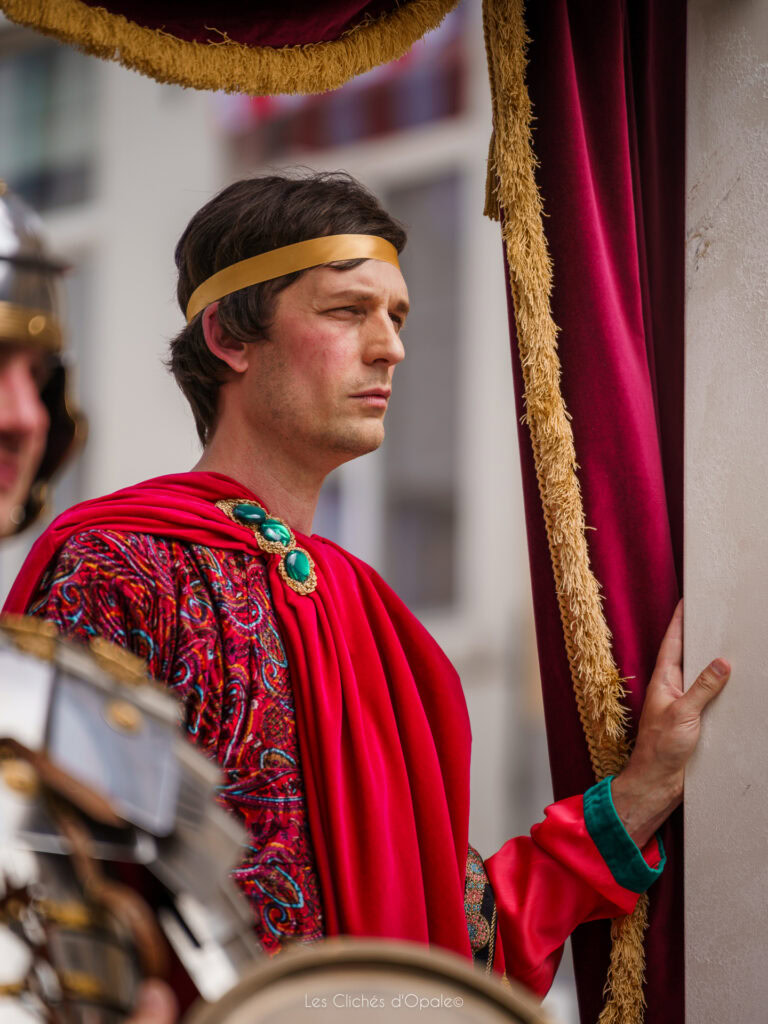 Homme en costume romain avec toge rouge et accessoires lors d'une reconstitution historique.