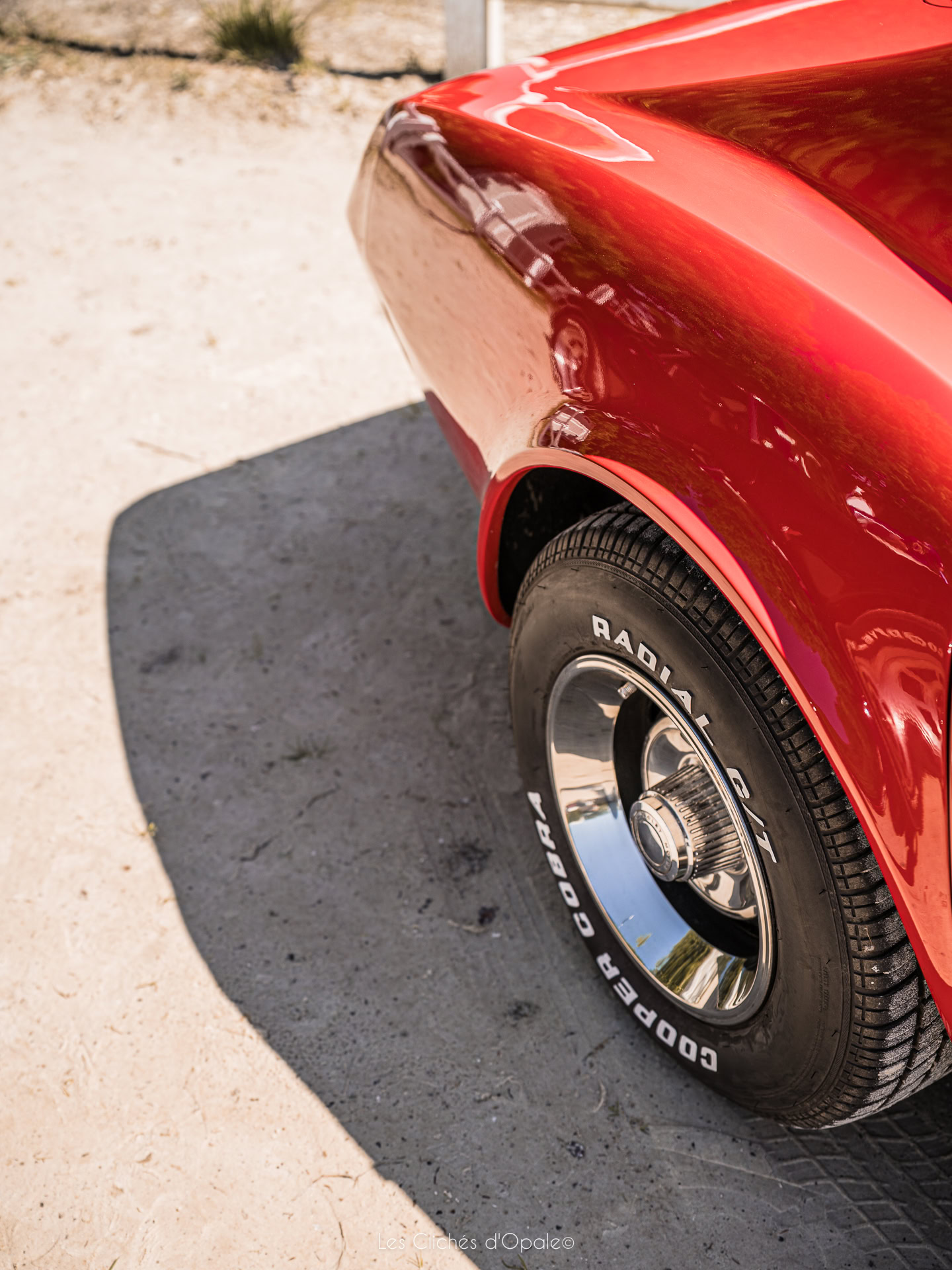Voiture classique rouge avec roue en chrome et pneu à flanc blanc.