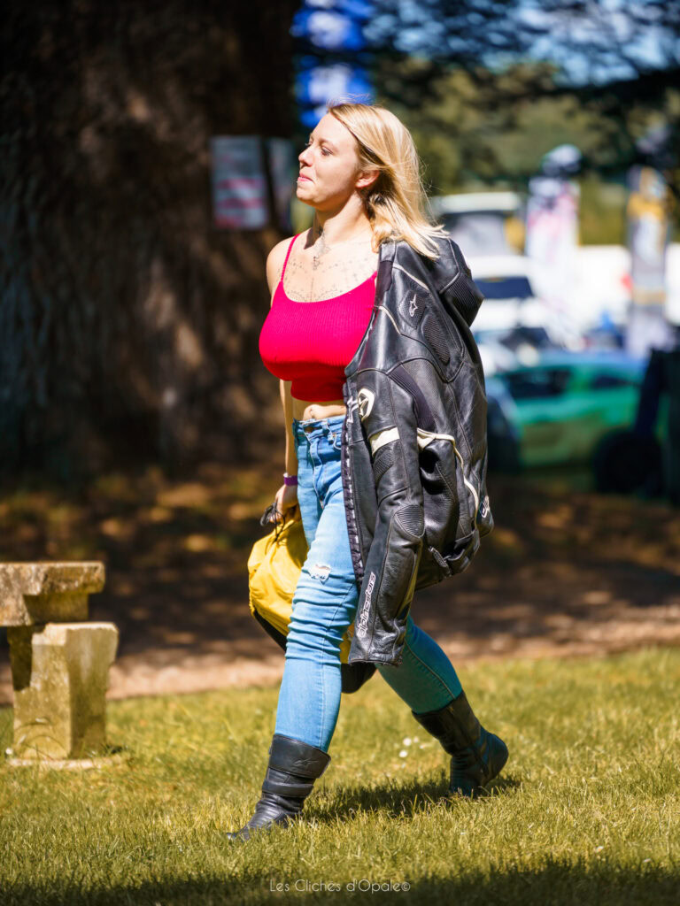 Femme en tenue décontractée avec veste en cuir, marchant dans un parc ensoleillé.
