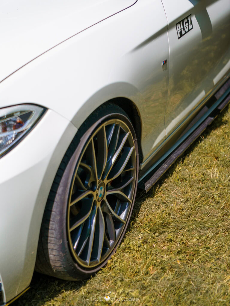 Voiture sportive blanche avec jantes noires, vue de côté sur herbe.